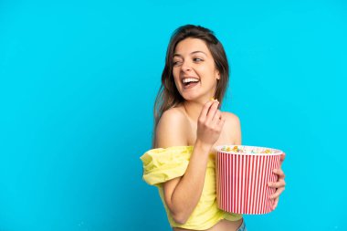 Mavi arka planda izole edilmiş beyaz bir kadın elinde koca bir kova patlamış mısır tutuyor.