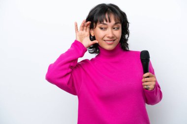 Genç Arjantinli şarkıcı kadın, beyaz arka planda izole edilmiş bir şekilde elini kulağına koyarak bir şeyler dinliyor.