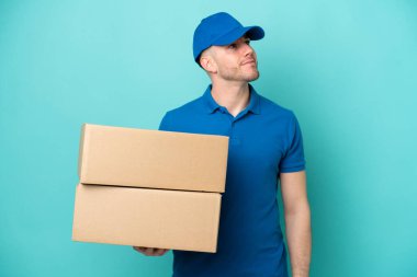 Teslimat yapan beyaz adam mavi arka planda izole edilmiş bir şekilde yukarı bakarken bir fikir düşünüyor.