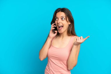 Mavi arka planda izole edilmiş cep telefonu kullanan beyaz bir kadın çözümü bulmak için parmağını kaldırıyor.