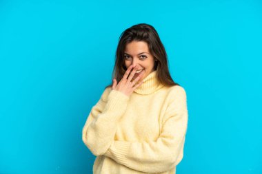 Mavi arka planda izole edilmiş genç beyaz kadın mutlu ve gülümsüyor.