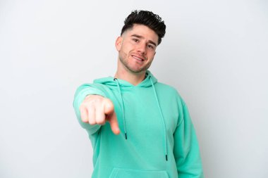 Beyaz arka planda izole edilmiş genç beyaz adam mutlu bir ifadeyle ön tarafı işaret ediyor.