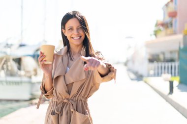 Dışarıdaki genç bir kadın açık havada kahvesini yudumlarken kendine güvenen bir ifadeyle seni işaret ediyor.