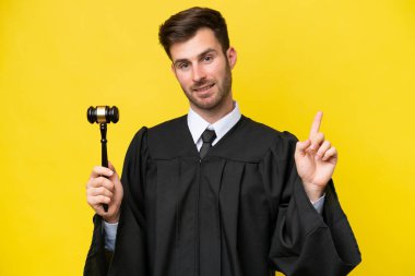 Kafkasyalı yargıç sarı arka planda izole edilmiş ve en iyinin işareti olarak parmağını kaldırıyor.