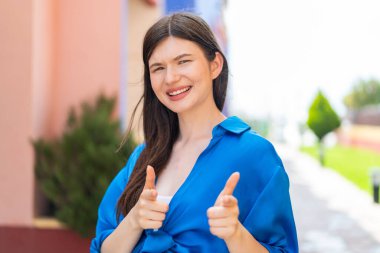 Açık havada genç ve güzel bir kadın ön tarafı gösteriyor ve gülümsüyor.