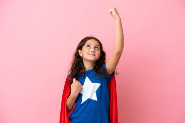 Küçük beyaz kız pembe arka planda izole edilmiş süper kahraman kostümlü ve zaferi kutluyor.
