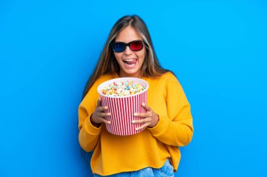 Mavi arka planda 3 boyutlu gözlüklü ve elinde koca bir kova patlamış mısır tutan beyaz bir kadın.