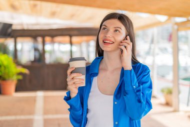 Dışarıda cep telefonu kullanan ve elinde kahve tutan genç ve güzel bir kadın.