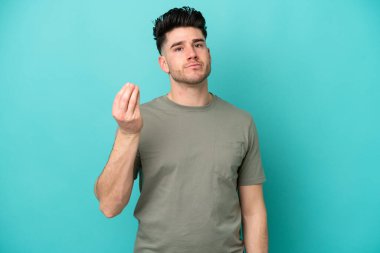 Mavi arka planda izole edilmiş genç beyaz adam İtalyan jestleri yapıyor.