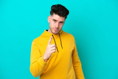 Mavi arka planda izole edilmiş genç beyaz adam hayal kırıklığına uğramış ve ön tarafı işaret ediyor.