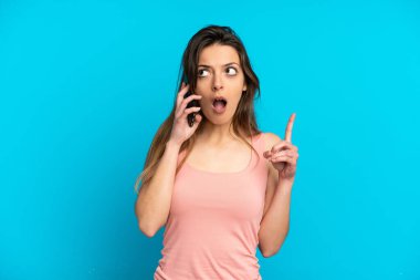 Mavi arka planda izole edilmiş cep telefonu kullanan genç beyaz kadın bir fikri işaret ederek...