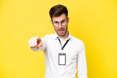 Sarı arka planda izole edilmiş, şaşırmış ve ön tarafı işaret eden genç bir beyaz.