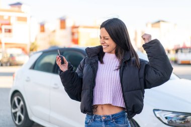 Açık havada elinde araba anahtarlarıyla genç bir kadın zaferi kutluyor.
