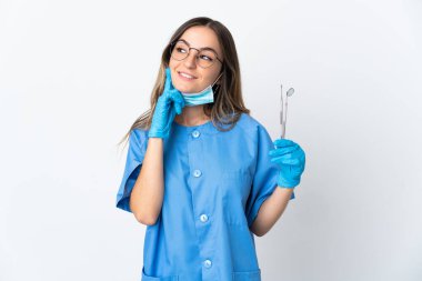 Romen kadın diş hekimi pembe arka planda izole edilmiş araçları tutarken, bir yandan da yukarı bakarak bir fikir üretiyor