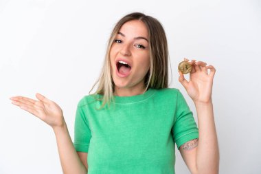 Elinde Bitcoin tutan genç Romen kadın beyaz arka planda şok olmuş yüz ifadesi ile izole edilmiş