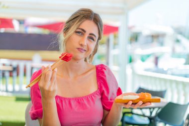Açık havada sashimi tutan genç sarışın kadın.