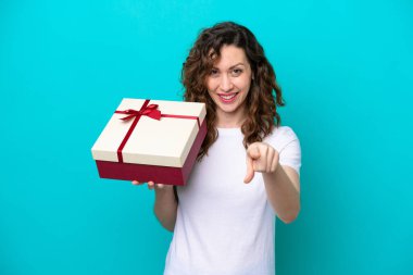 Elinde mavi arka planda izole edilmiş bir hediye tutan beyaz bir kadın kendinden emin bir ifadeyle seni işaret ediyor.