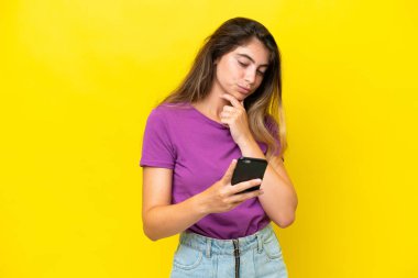 Genç beyaz kadın sarı arka planda izole edilmiş düşünüyor ve bir mesaj gönderiyor.