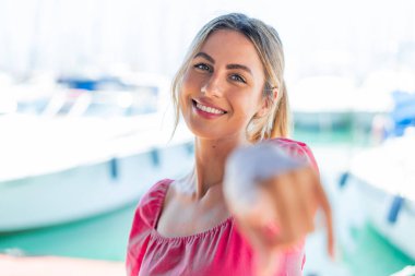 Açık havadaki genç sarışın kadın kendine güvenen bir ifadeyle seni işaret ediyor.