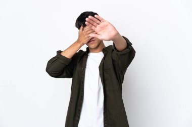İzole edilmiş beyaz arka planı olan genç bir adam jesti durdurup yüzünü kapatıyor.
