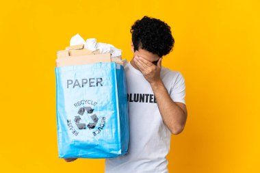 Genç Venezuelalı bir adam elinde kağıt dolu bir geri dönüşüm çantası tutuyor yorgun ve hasta bir ifadeyle geri dönüşüm yapmak için.