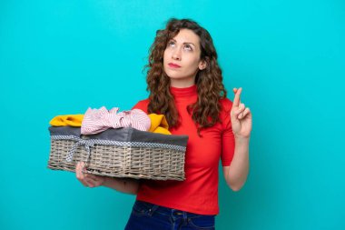 Mavi arka planda izole edilmiş çamaşır sepetini tutan beyaz bir kadın, şans diliyor.