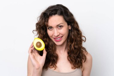 Beyaz arka planda izole edilmiş beyaz bir kadın elinde bir avokado tutarken gülümsüyor. Portreyi kapat