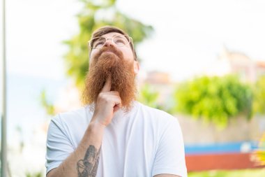 Kızıl saçlı, sakallı, gözlüklü ve yukarı bakan adam.