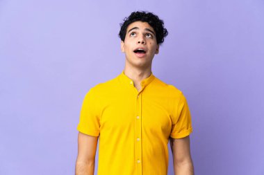 Genç Venezuelalı adam mor arka planda izole edilmiş yukarı bakıyor ve şaşırmış bir ifadeyle