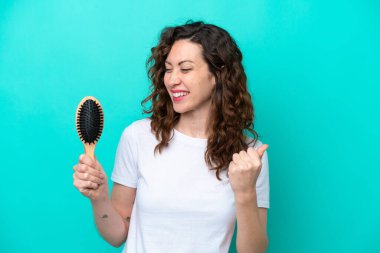 Mavi arka planda saç fırçası tutan beyaz bir kadın zaferi kutluyor.