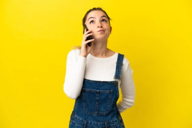 İzole edilmiş sarı arka planda cep telefonu kullanan genç bir kadın.