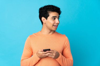 Venezüellalı adam mavi arka planda cep telefonu kullanarak izole edilmiş.