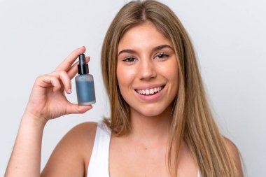 Beyaz arka planda izole edilmiş beyaz bir kadın elinde bir serum tutarken gülümsüyor. Portreyi kapat