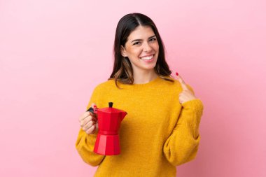Pembe arka planda izole edilmiş kahve makinesini tutan genç bir İtalyan kadın baş parmak işareti yapıyor.