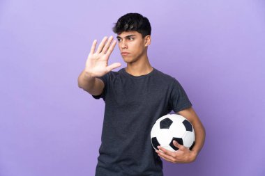 İzole edilmiş mor arka planda genç futbolcu dur hareketi yapıyor ve hayal kırıklığına uğruyor.