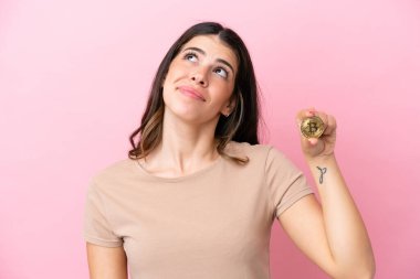Pembe arka planda izole edilmiş Bitcoin tutan genç İtalyan kadın.