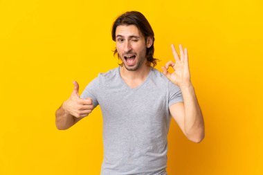 Sarı arka planda izole edilmiş genç yakışıklı işaret ve baş parmak işareti gösteriyor.