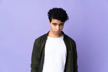 Genç Venezuelalı adam üzgün bir ifadeyle mor arka planda izole edilmiş.