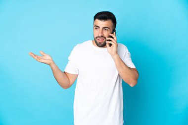 İzole edilmiş mavi arka planı olan beyaz bir adam cep telefonuyla sohbet ediyor.