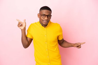 Pembe arka planda izole edilmiş genç latin adam parmak uçlarını işaret ediyor ve mutlu.