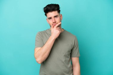 Kafkasyalı genç adam mavi arka planda soyutlanmış düşünüyor.