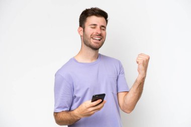 Beyaz arka planda izole edilmiş genç beyaz bir adam ve telefon zafer pozisyonunda.