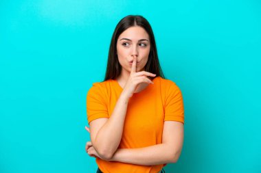 Mavi arka planda izole edilmiş beyaz bir kadın sessiz bir jest işareti gösteriyor. Parmağını ağzına sokuyor.