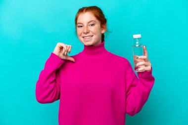 Mavi arka planda bir şişe suyu olan beyaz, genç bir kadın gururlu ve kendini beğenmiş.