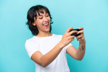 Genç Arjantinli kadın mavi arka planda izole edilmiş cep telefonuyla oynuyor.