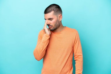 Kafkasyalı genç adam mavi arka planda izole edilmiş, baş ağrısı var.
