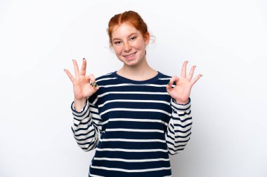 Beyaz arka planda izole edilmiş genç kızılımsı bir kadın iki eliyle tamam işareti gösteriyor.