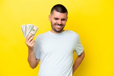 Kafkasyalı genç bir adam sarı arka planda izole edilmiş bir sürü para alıyor.