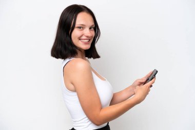 Beyaz arka planda izole edilmiş genç beyaz kadın cep telefonuyla mesaj ya da e-posta gönderiyor.