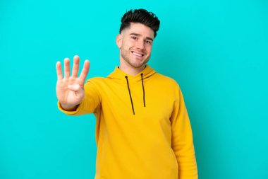 Mavi arka planda izole edilmiş genç beyaz adam mutlu ve parmaklarıyla dört tane sayıyor.